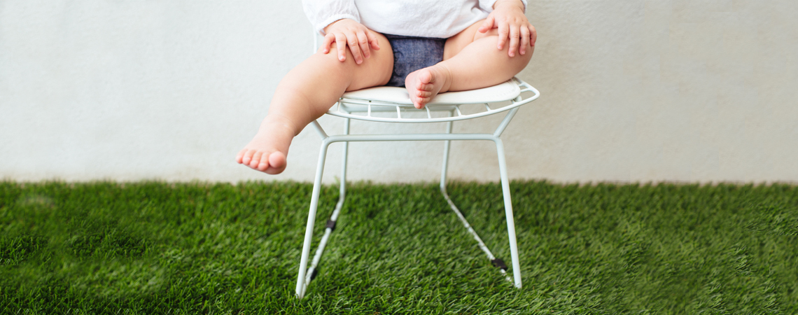 A baby girl sits on a Bertoia side chair.